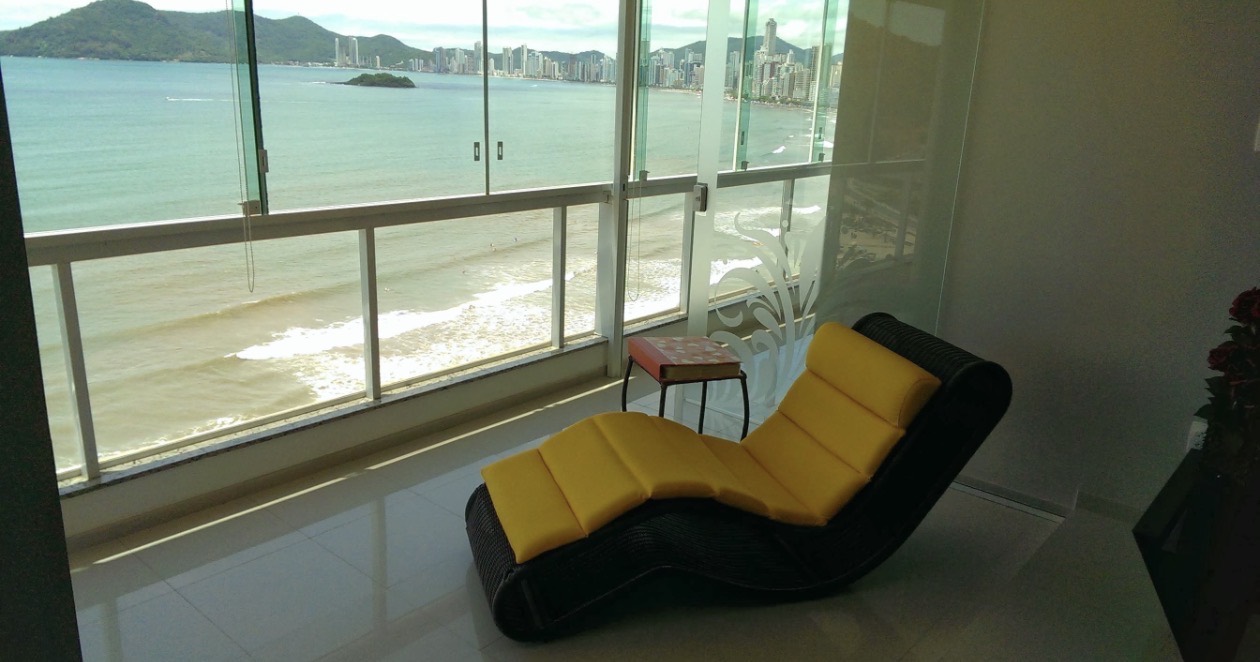 Yellow lounge chair facing the Balneário Camboriú coastline in an earlier daytime photograph